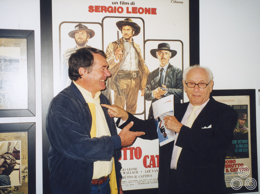 Renato Casaro stands with the actor Eli Wallach whom the artist depicted on the 1969 Italian re-release poster for The Good, The Bad and The Ugly, which can be seen behind them.